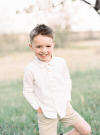 Young boy smiling in grassy field during Denver family photo session.