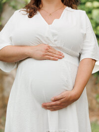 Close up image of a woman holding her growing pregnant belly in a white dress