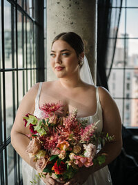 Close up portrait of bride standing by a window holding large pink bouquet