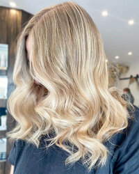 Soft blonde waves with luminous shine and subtle balayage, displayed in a professional salon setting.