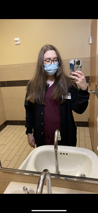 Lexi standing in the work bathroom wearing a face mask taking a selfie with fuzzy hair