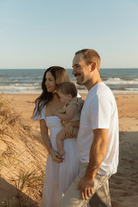 mom dad and daughter on beach during lifestyle photo session in prince edward island