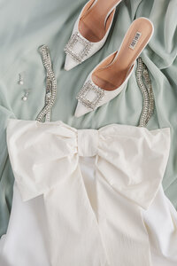 White wedding details flatlay with dress, shoes, and pearl drop earrings