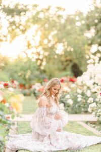 A maternity session photographed by Bay area photographer shows an expecting mother holding her baby bump dreaming and sitting in a rose garden.