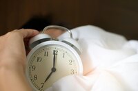 Woman holding an alarm clock in bed