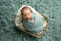 sleeping newborn baby wearing hat posed in basket with white  blanket