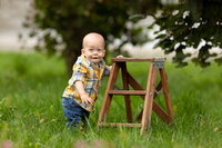 ONe year old boy outside standing up holding a mini ladder