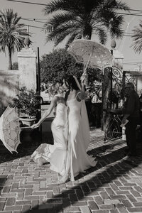 A photo of a bride and a friend posing for a photo with umbrellas in New Orleans 