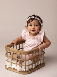 one year old girl in pink sitting in basket for cake smash session
