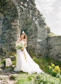 a bride standing next to an old castle during their ireland elopement