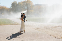 A newlywed couple dancing together in sprinklers 