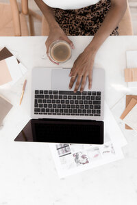 black woman's hand holding a cup of coffee and typing on laptop