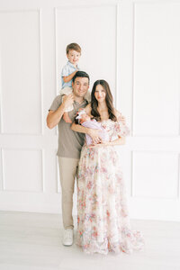 mom holding newborn baby, dad, toddler son on dads shoulders standing in Phoenix Arizona studio.