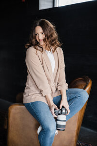 Woman sitting on a leather chair holding a camera, with a gentle smile, is an esteemed photography mentor.