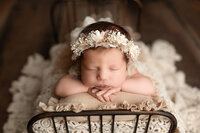 Baby girl posed on a newborn bed wearing a beautiful white floral crown.
