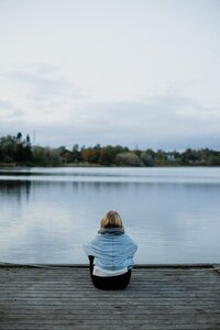 mielen paremminvoinnin ja kehomieliyhteyden valmentaja istuu laiturilla  katsoen sinistä järvimaisemaa