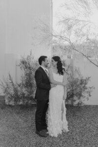 Bride wearing luxury wedding dress and groom standing in front of desert landscaping at backyard wedding.