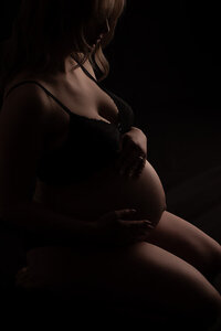 maternity portrait.  Expecting mother is posed on a black backdrop and backlit to create a silhouette of the baby bump.