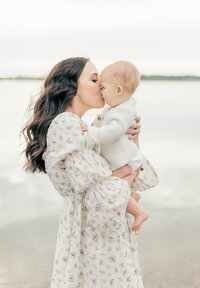 Mother kisses her 6-month-old baby girl while holding her as they stand on the shore of a Kansas City lake. 