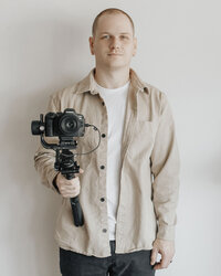 Josh McElroy standing in front of white wall and holding camera
