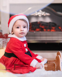Little girl in red sitting near Christmas tree in Calini Weddings Studio – magical winter portrait with gift boxes and festive decorations.