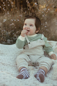Toddler in overalls sitting on a blanket.