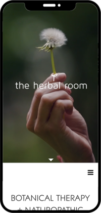 A hand holds a dandelion against a blurred natural background. Text reads "the herbal room," conveying a calm, natural, and organic tone.