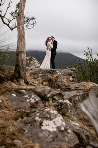 Black and White photograph of a bride and groom running in a field looking happy on wedding day.
