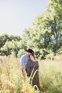 Grassy field Maternity photo of husband and wife with midday sun in a cowboy hat in Russellville, Ohio.