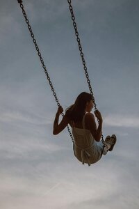 A woman is captured in a moment of carefree joy, soaring on a swing against a soft sky.