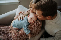 Baby laying on mom's arm and dad is giving him a kiss