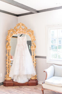 A wedding dress hangs on an ornate gold mirror in the Key Rose Estate bridal suite.