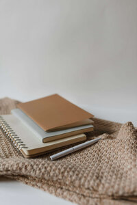 Image of a stack of small journals and a pen on a blanket