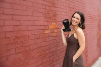 halea smiling in a brown dress while holding a professional camera