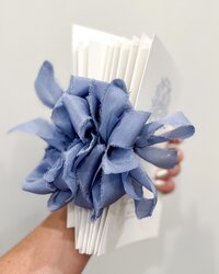 A person holding a stack of wedding programs that feature a dusty blue bow tied.