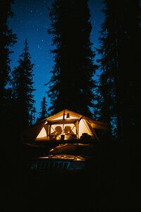 silhouette of a couple about to kiss in a rooftop tent on top of a jeep in the middle of a forest with a starry blue sky above