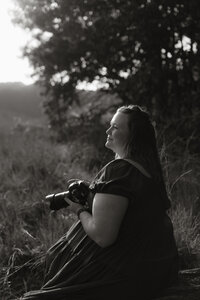 Jessica, an associate photographer for Rainstorm Photo & Video, smiling while holding her camera in the field during sunset, part of the creative team behind the brand’s cinematic wedding storytelling.