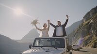 Couple holding up hands in celebration while in jeep after eloping