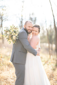 Bride and Groom smiling as they squeeze eachother ourside of Fields Reserve in Stoughton WI on their Wedding Da7