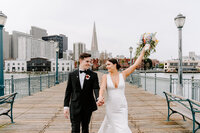 Newlyweds walking along pier celebrating.