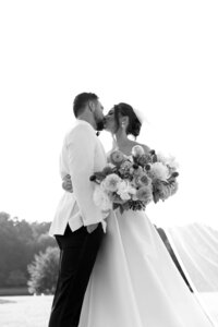 Elegant black and white photoshoot capturing a romantic kiss between the bride and groom against the scenic beauty of nature