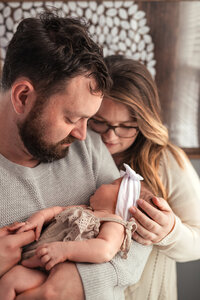 Dad holds his new baby, as mom and dad both look down at baby girl during a newborn home session