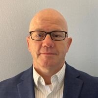 Dave Dessart, A Harley Davidson Organization + Development Director, smiles in his headshot. He's bald, wearing glasses, a white shirt, and blue suit jacket