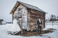 A couple poses by an old farmhouse in the Swedish Arctic after their wedding.