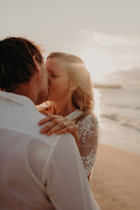 Bride kissing her husband on the beach at sunset