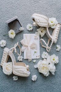 Stylish flatlay with bridal shoes, wedding invitation, and fresh white flowers arranged on soft fabric background