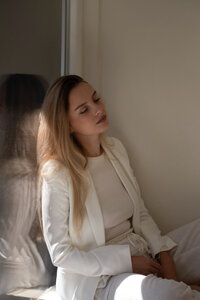 Woman in a white suite leaning against a window 