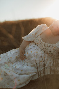 Pregnant mom sitting in a grassy field during golden hour while smiling with eyes closed in Murrieta, CA.