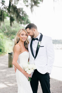 A radiant bride in a strapless gown and a groom in a white tuxedo share a romantic moment at their luxury wedding on Sea Island. A timeless coastal celebration.