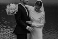 Bride and groom snuggle together in front of a lake